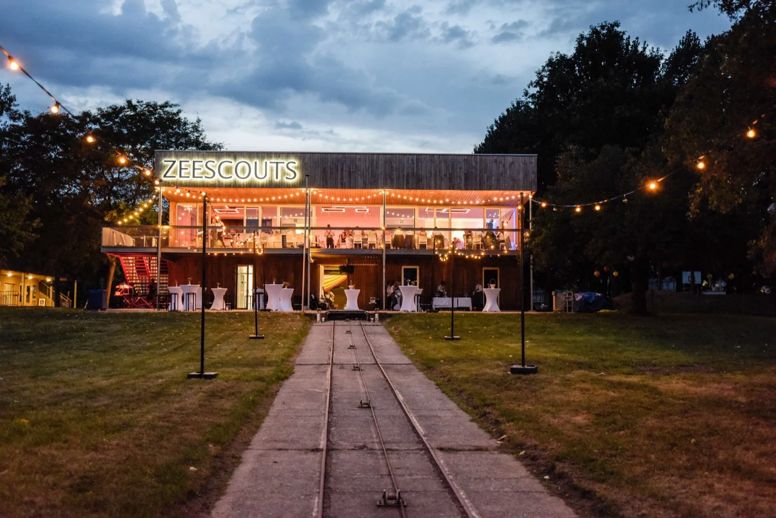 Pier 165 bij valavond, met lichtslingers langs het pad naar de zaal